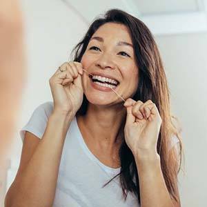 Smiling woman flossing to prevent toothache in Houston