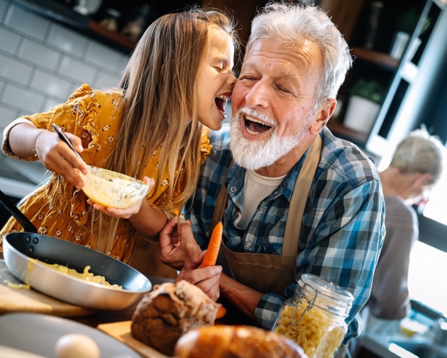 An older man in the kitchen with his granddaughter smiling after receiving implant dentures in Houston