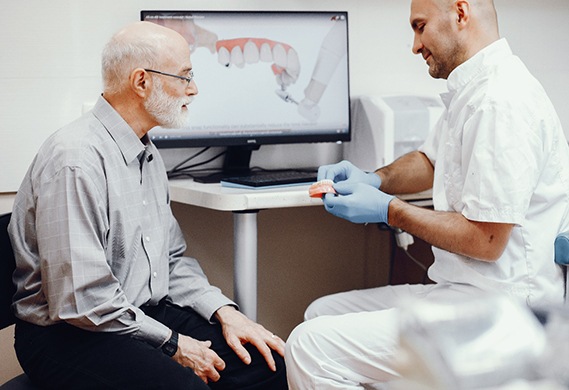 An older male patient listening as his dentist discusses his eligibility for implant dentures in Houston