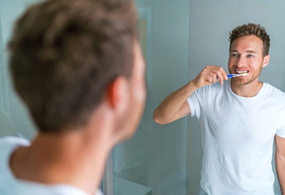 person brushing their teeth while looking in the bathroom mirror